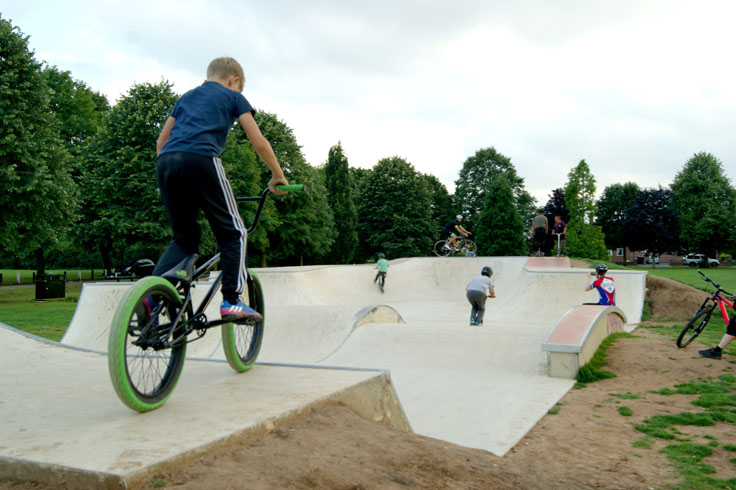 A group of children on bikes and scooters riding up and down bike ramps.